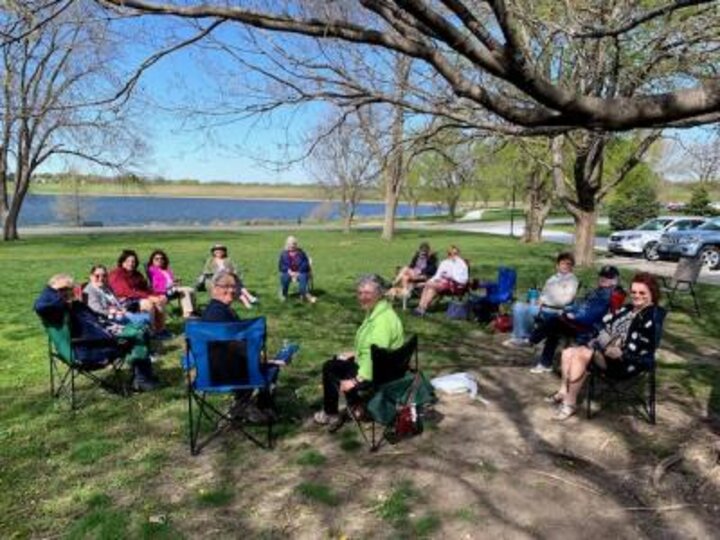 Club members in lawn chairs in grassy field look at camera.