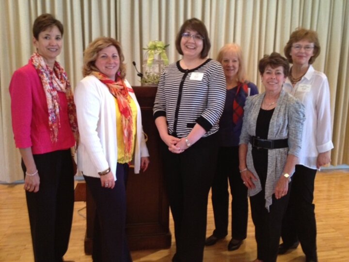 Six club members pose for photo in front of podium.