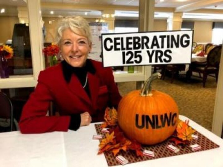 Woman poses in front of pumpkin with UNLWC stenciled on it with sign reading 'Celebrating 125 Years'.