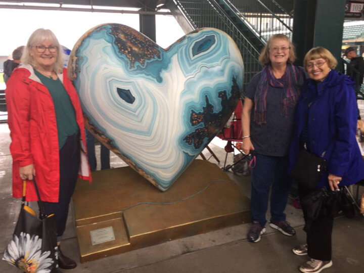 Three women pose next to Lincoln Arts Program heart sculptures.