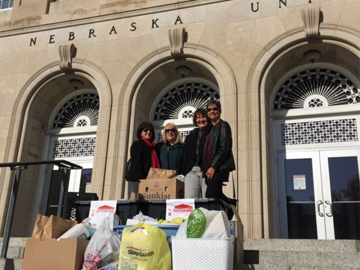 Four women pose behind a large pile of food on the steps of the Nebraska Union.
