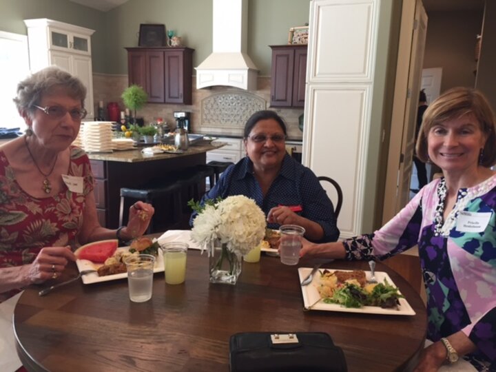 Three women sitting at kitchen table with plates of food smile for photo.