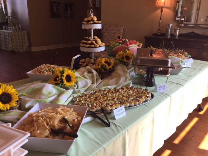 Long table of food garnished with sunflower bouquets.