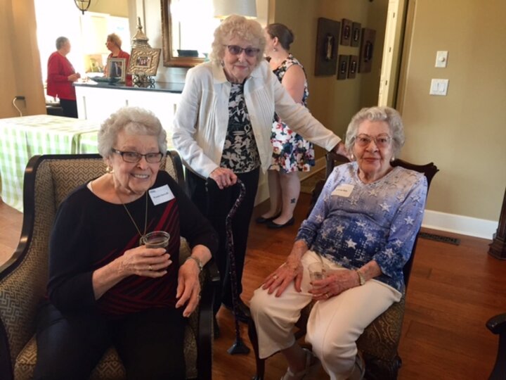 Three women inside home pose for photo with women in the background.