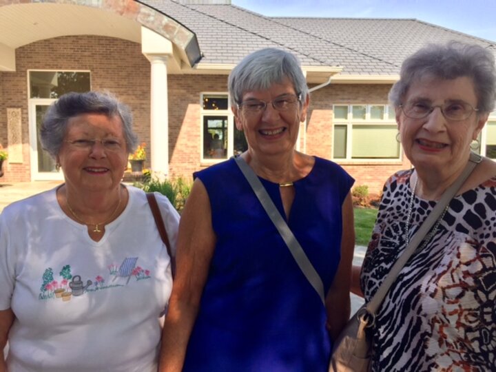 Three women outside of large home pose for photo.