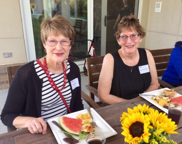 Two women sitting at picnic table with plates of food in front of them.