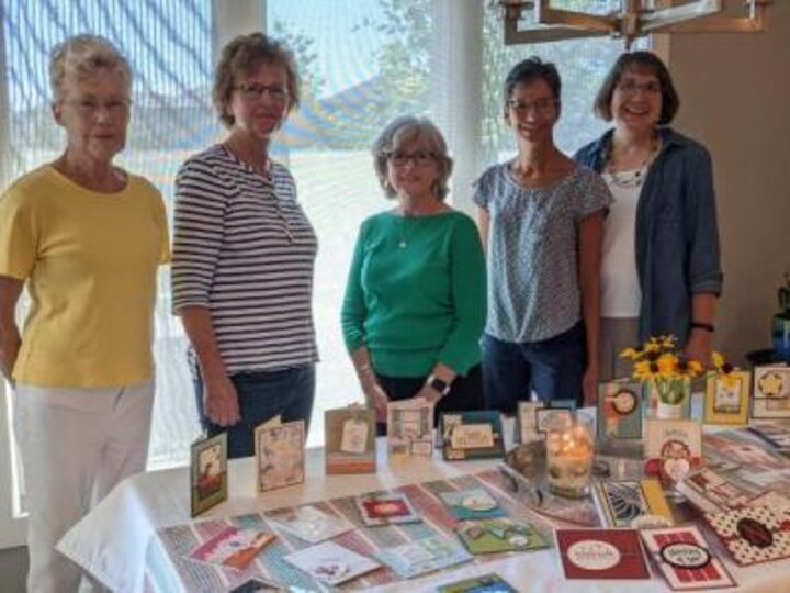 Five women stand behind table covered in greeting cards.