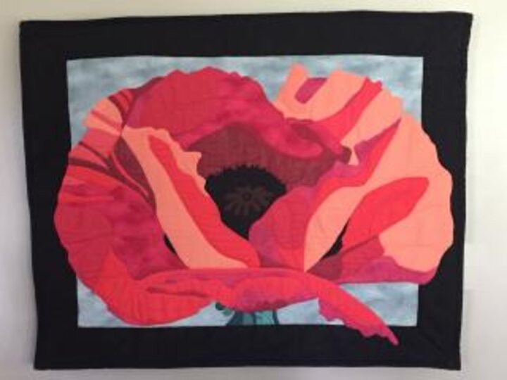 A beautiful quilt picturing a large red and pink poppy flower.