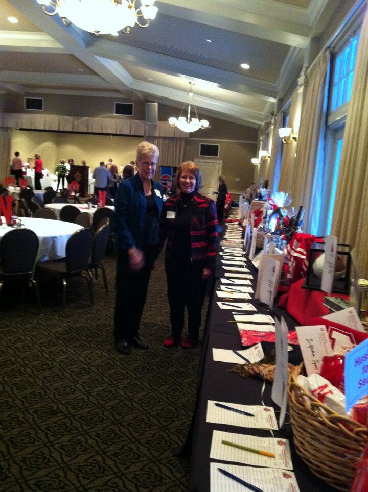 Banquet room with two club members standing near long table lined with auction items.
