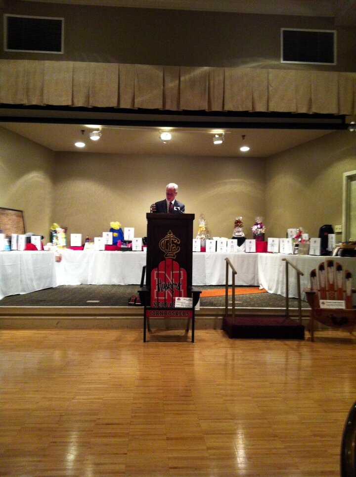 Man at podium with tables of auction items in the background.