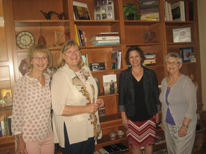 Four women pose in front of built in shelves.