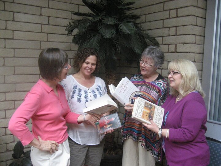 Four women pose with open books in their hands.