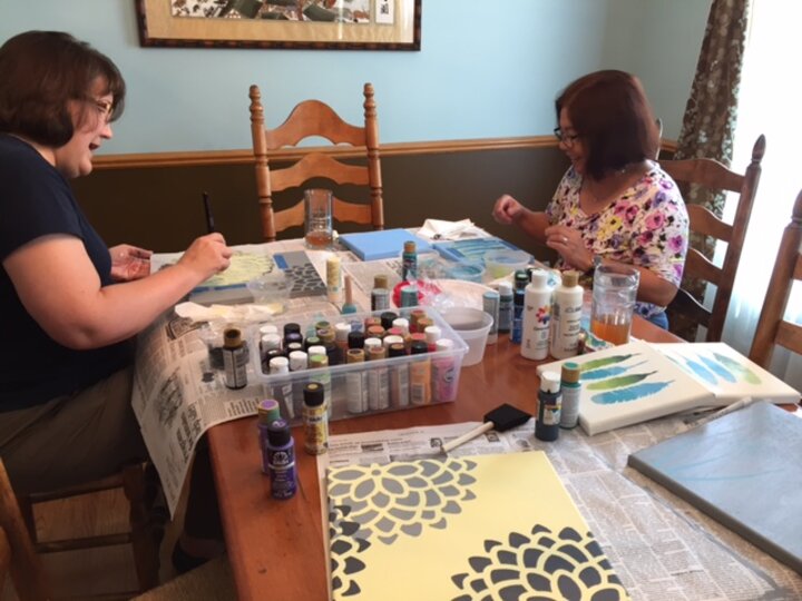 Two women seated across from each other painting craft projects.