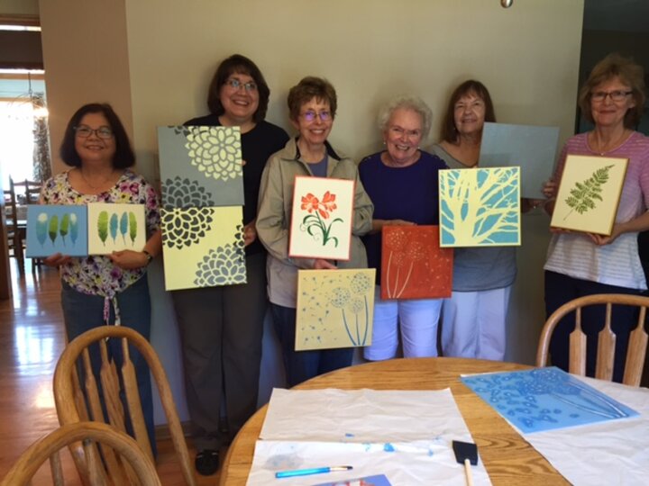 Six women showing off their paintings.