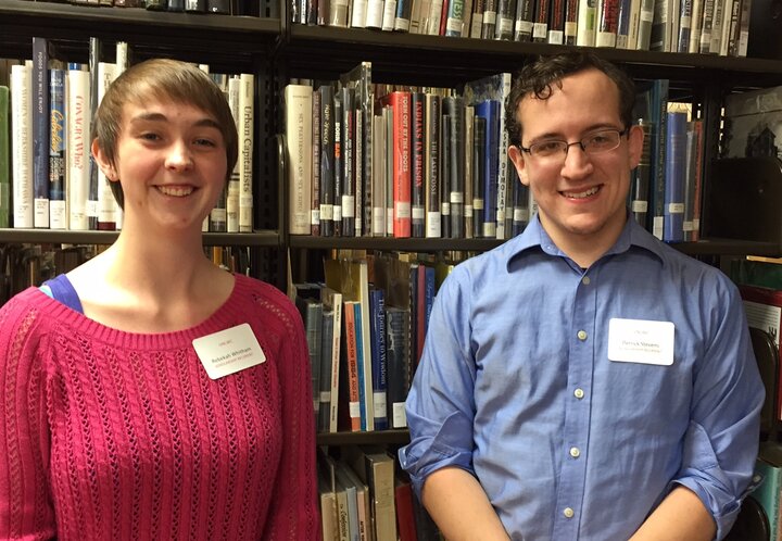 Man and woman pose for photo in front of shelves filled with books at library.