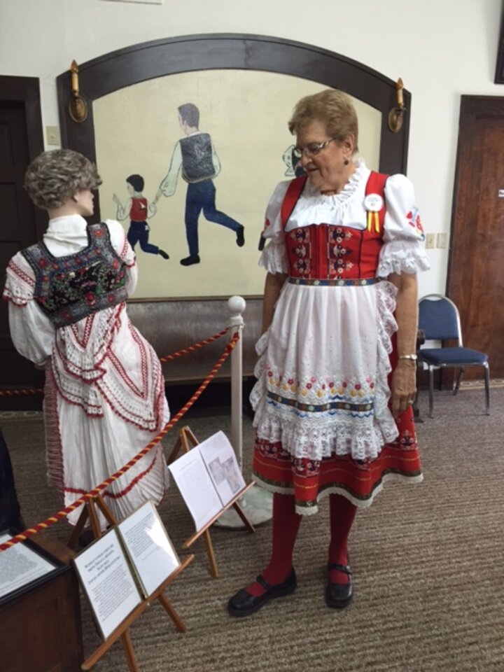 Woman in traditional European dress looks at mannequin in similar outfit.