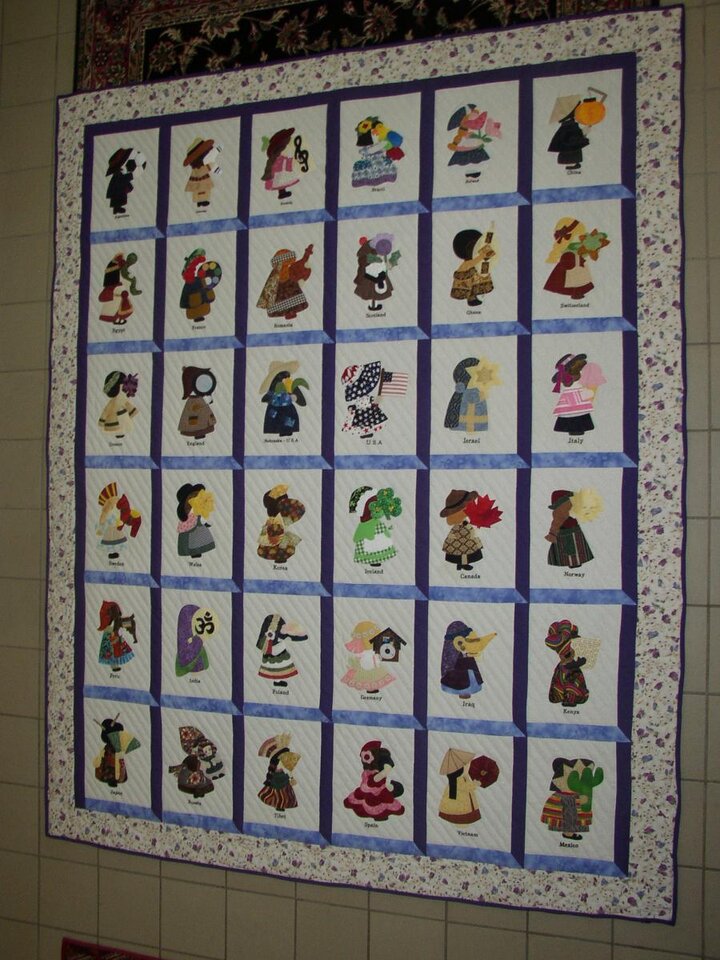 A beautiful quilt featuring small characters in a grid hangs on wall.