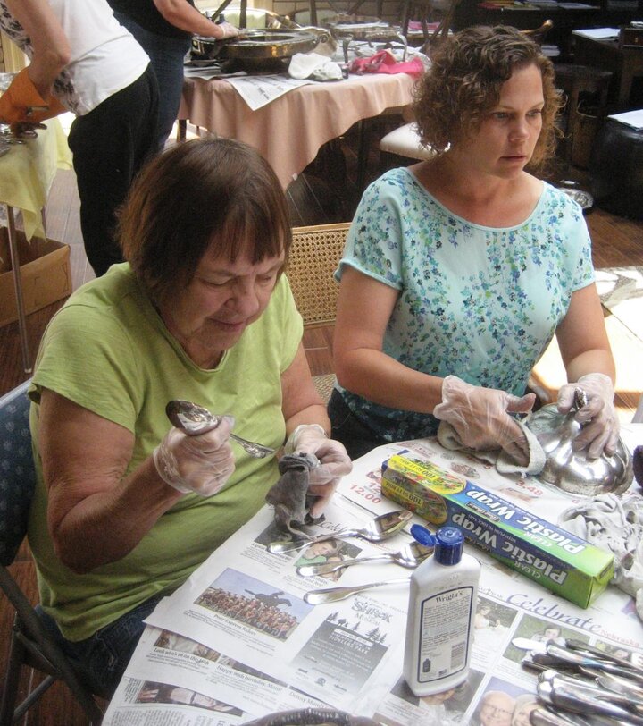 Two club members sit at table cleaning silver items