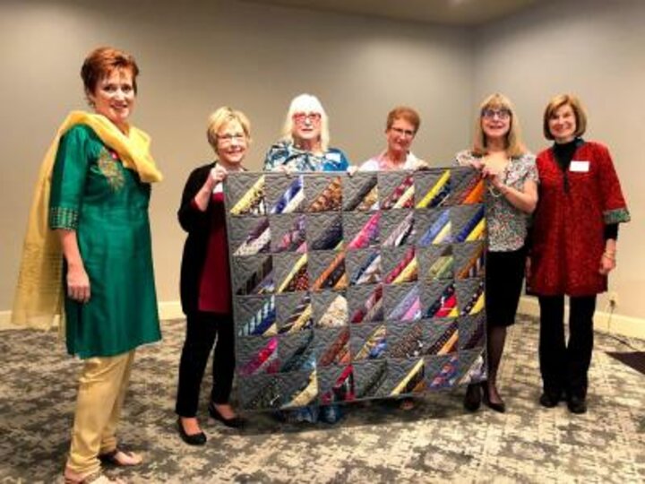 Six women showing off the silk tie quilt.