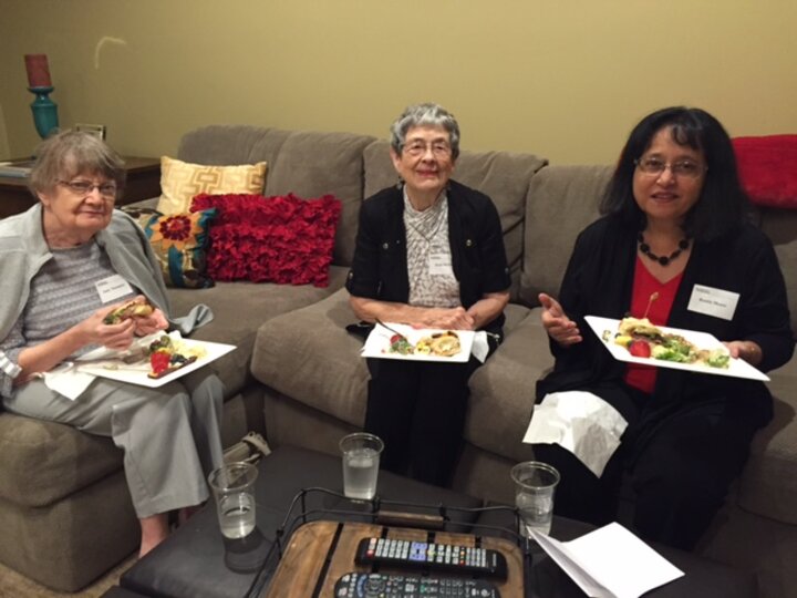 Three women seated eating, pose for photo.